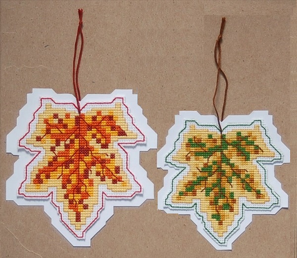A set of two speckled leaves stitched on white aida cloth. (the red on 14 ct and the green on 16ct) and backed with heavy-weight, fusible web then trimmed to shape and mounted on white, leaf-shaped backplates. Finishing instructions and backplates are included in the leaflet.  SRP  $16.00 Stitch count: 52w x 55h